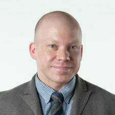 Portrait of a man with a slight smile as he looks directly into the camera. He is wearing a collared shirt, a tie and a suit jacket.
