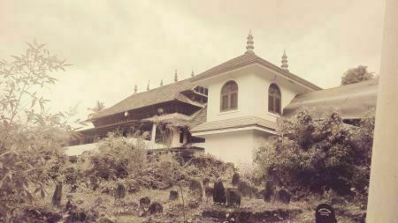 Black and white picture of a mosque in India with peaked roof amid trees.