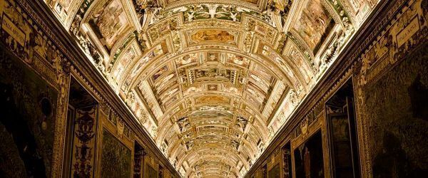 This image depicts the breathtaking vaulted ceiling of the Gallery of Maps within the Vatican Museums. The ornate corridor is renowned for its elaborate gold stucco work and vibrant frescoes that illustrate various religious and historical scenes.